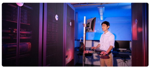 A computer science major stands at a computer in a server room